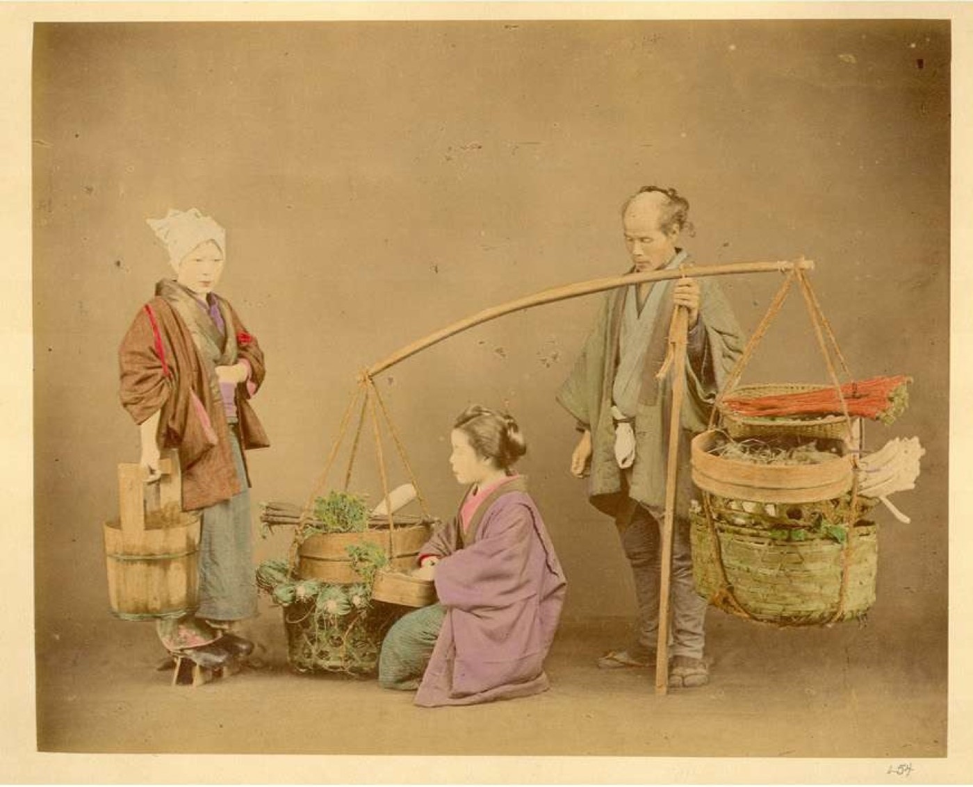 天秤棒で野菜籠を担ぐ行商人と、品定めをする客を写した明治初期の彩色写真